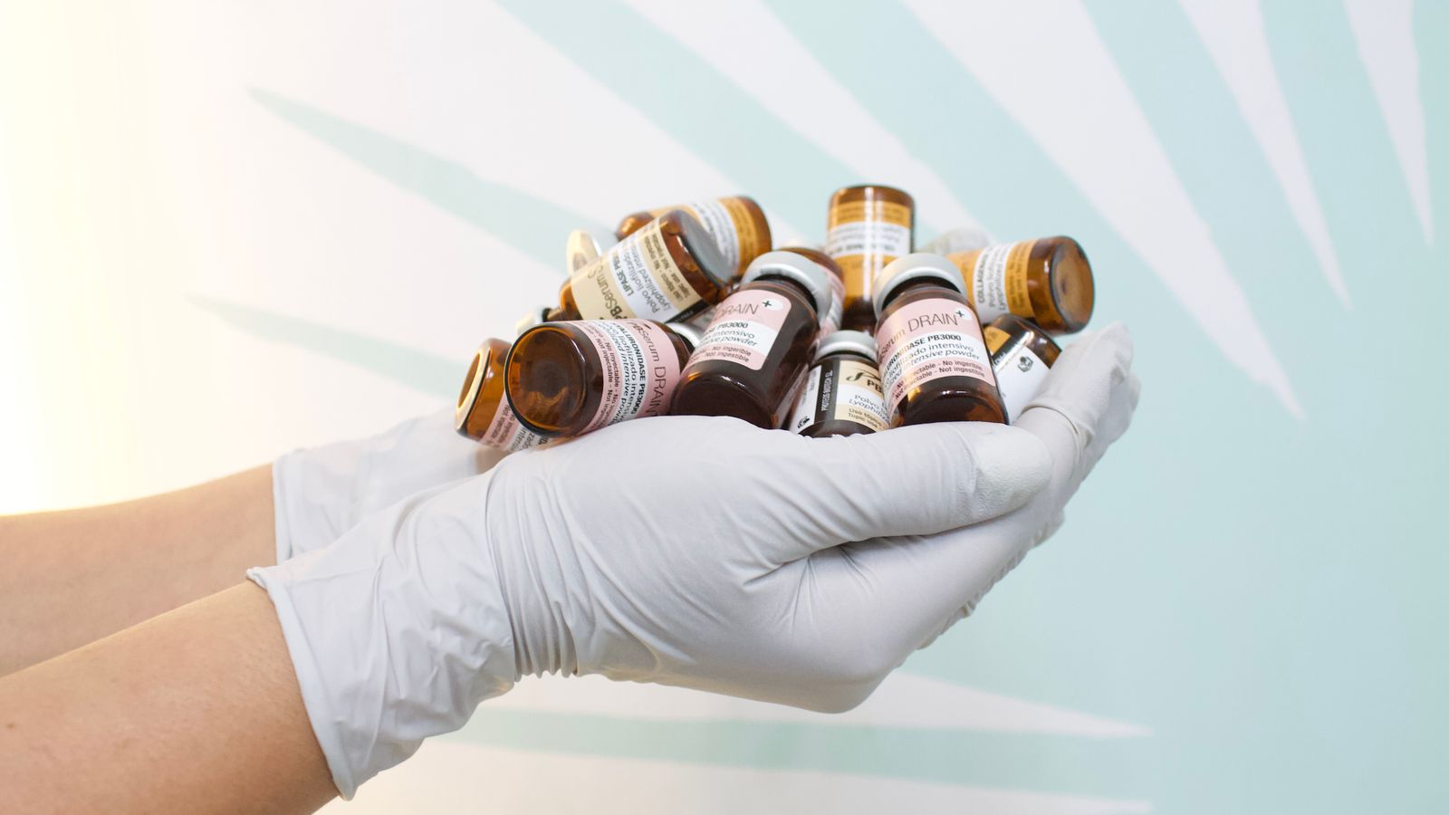 A close-up of gloved hands holding multiple medicine bottles against a light background.