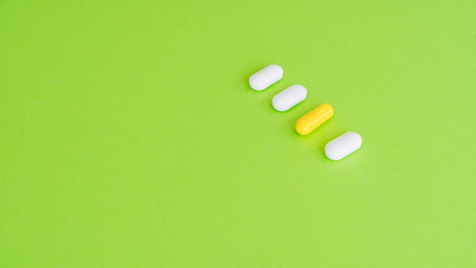 A row of white and yellow capsules arranged on a green surface.