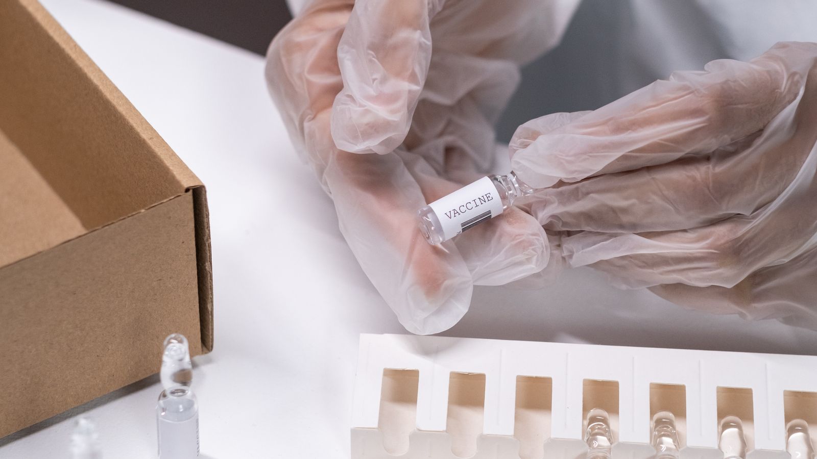 A gloved hand holding a small glass vial next to several other vials arranged on a clinical tray.