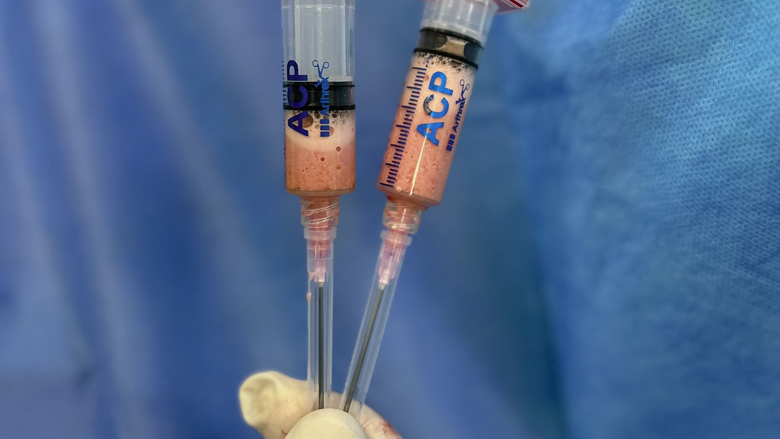 Close-up of a gloved hand holding a syringe with a clear substance against a blue background.