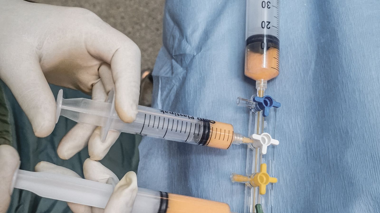 Close-up of multiple syringes and gloved hands on a lab bench during sample handling.